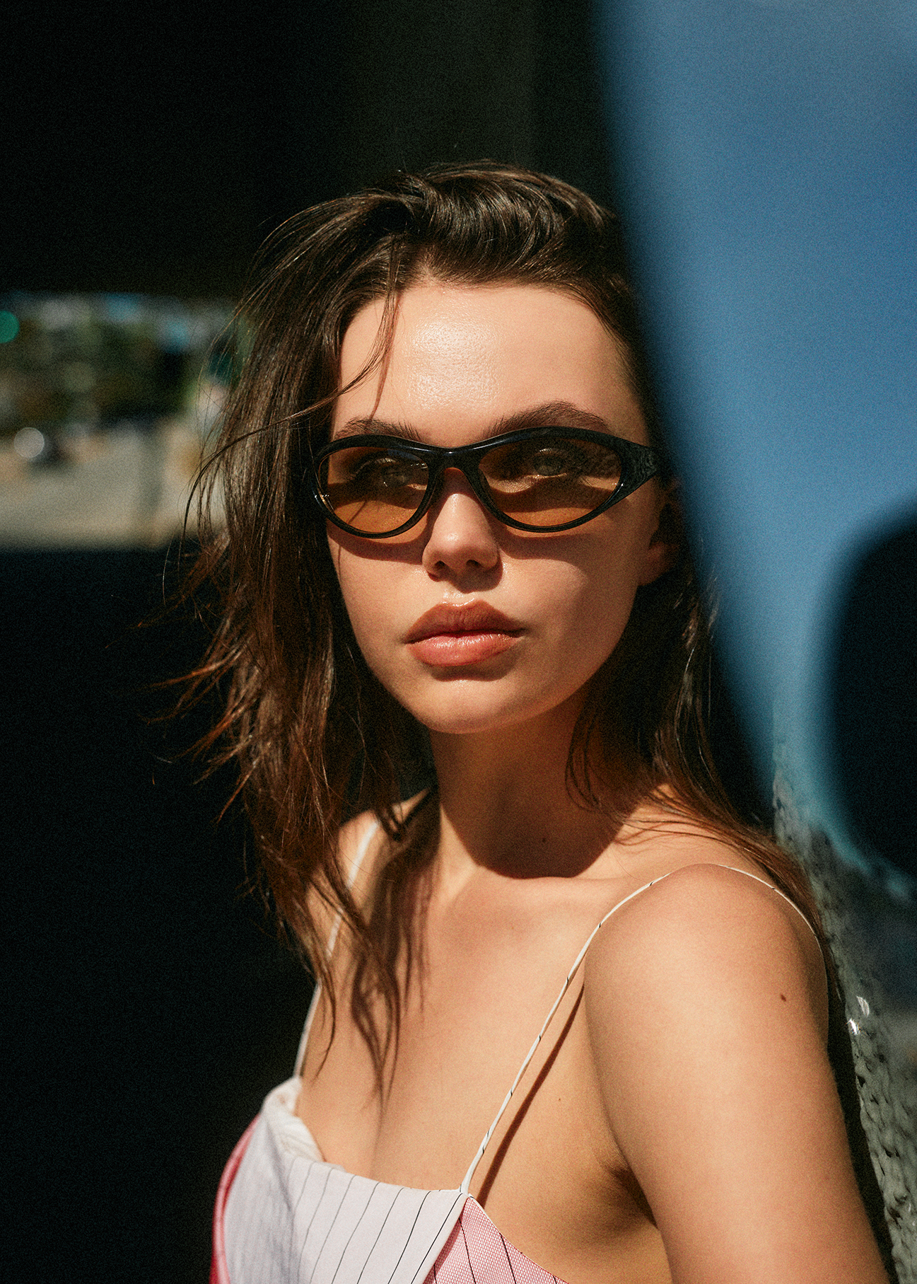  Portrait of Caroline Cummings in sunglasses with lips pursed making eye contact with the camera aganist a dark backdrop